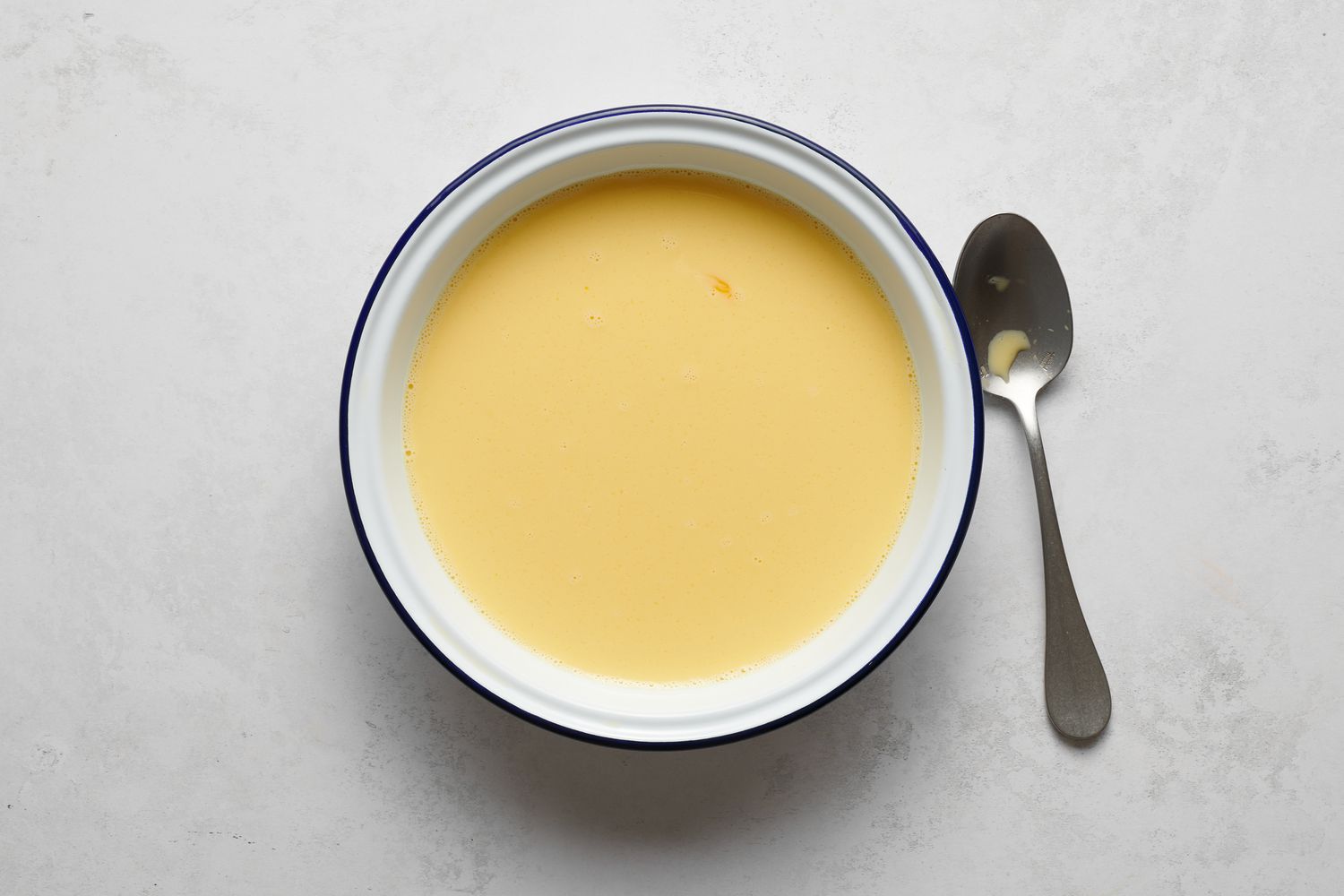 A bowl of whisked eggs, milk, sugar, and salt