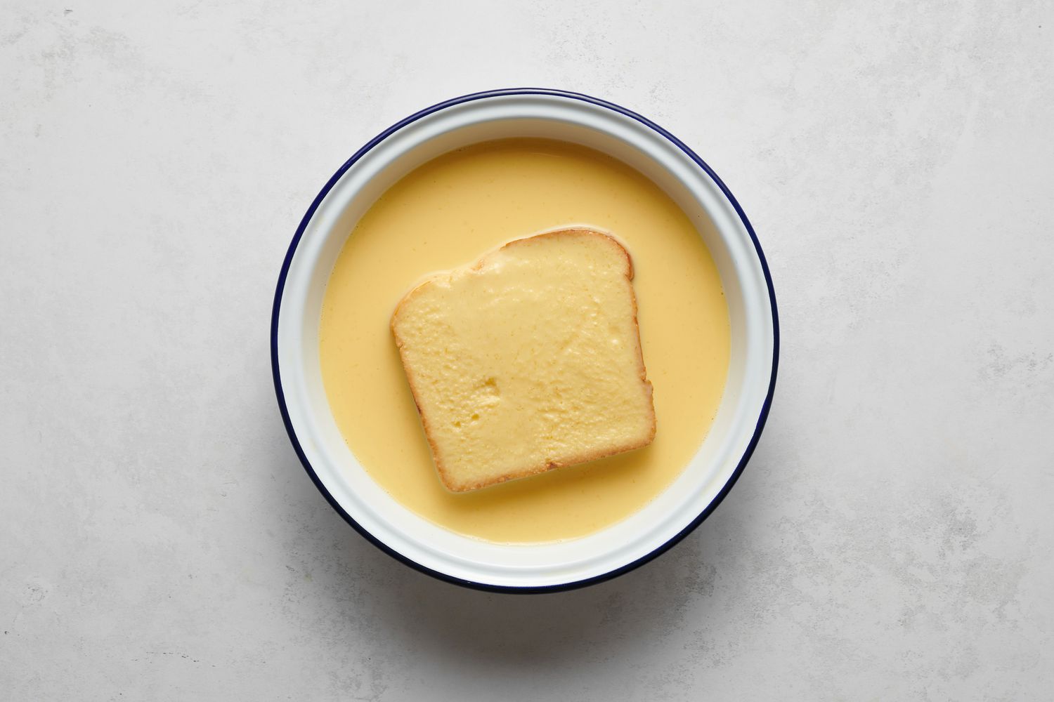 A piece of bread soaking in the whisked egg and milk mixture