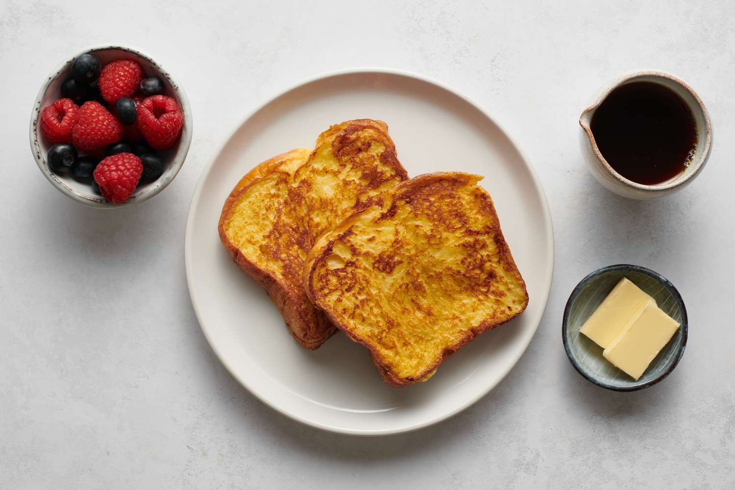 A plate of French toast served with butter, syrup, and berries